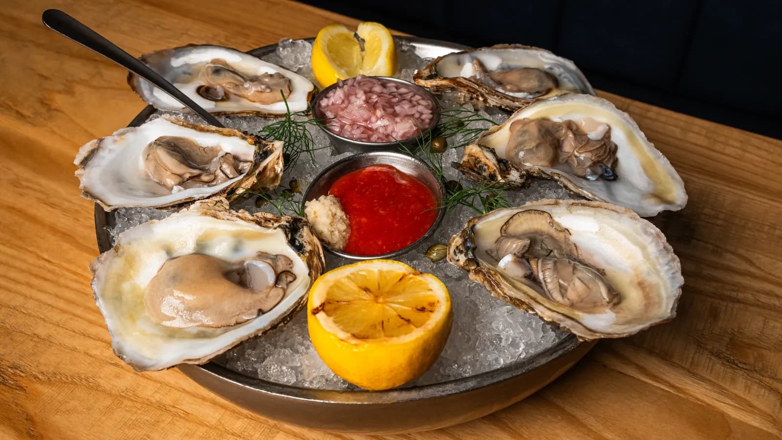 Platter of freshly shucked raw oysters on ice with mignonette, cocktail sauce and charred lemon at Seaside Oyster Bar